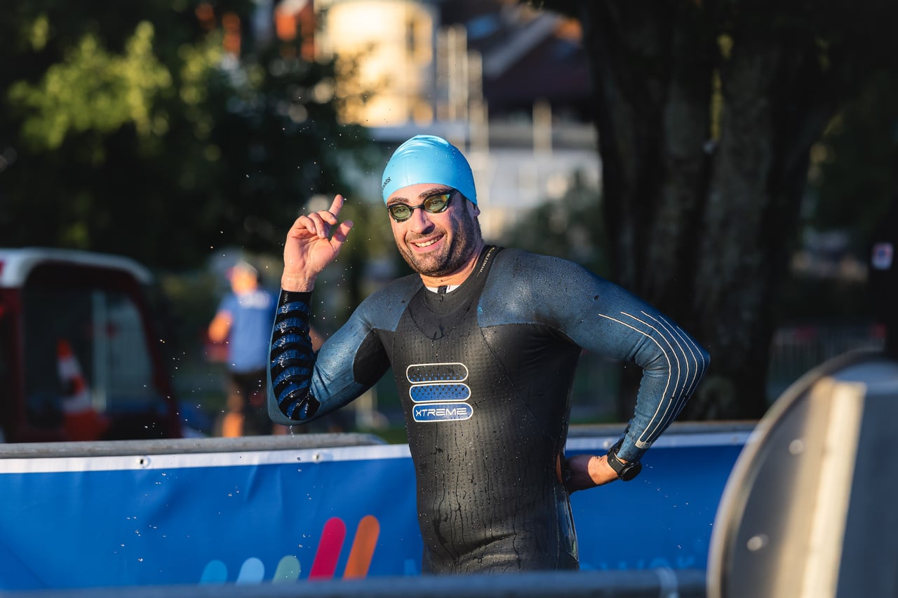 A triathlete in a wetsuit waves at the camera, Évian triathlon